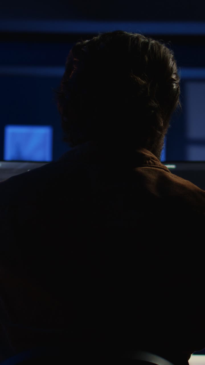 Uomo che programma su più monitor in un ufficio buio