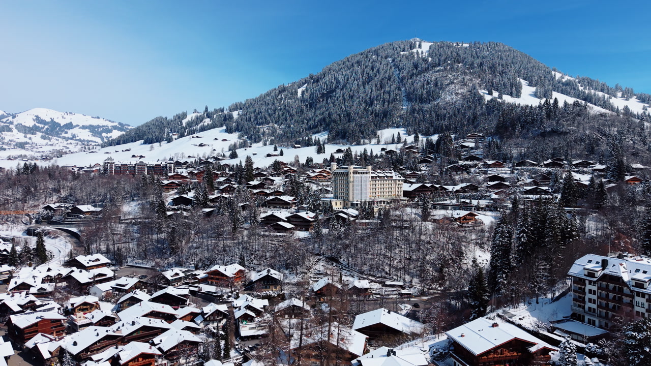Aerial: Gstaad Palace and snowy mountains during the day in Gstaad, Canton of Bern, Switzerland, push in drone shot