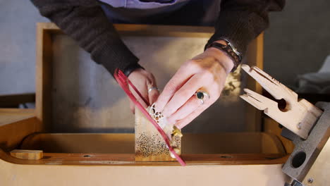 overhead close up of female jeweller working on brooch with saw in studio