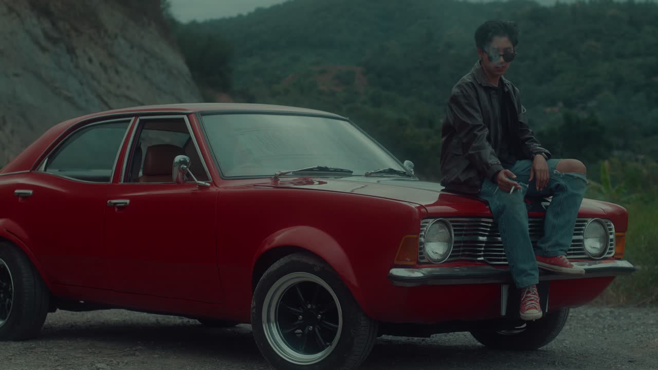 Uomo seduto sul cofano di un'auto d'epoca rossa