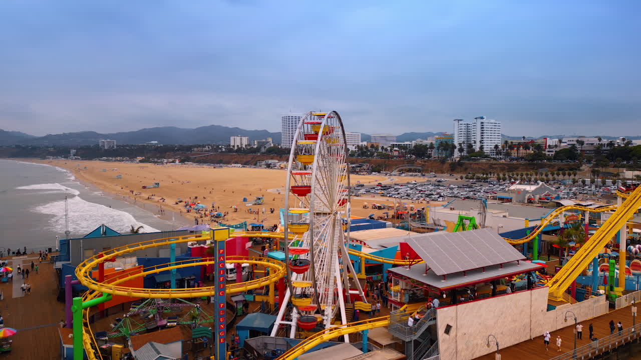 Los Angeles, USA, 29 August 2025: Footage around the Ferris Wheel in Pacific Park on the Santa Monica Pier. Numerous cars parked at backdrop. LA, California, USA on a gloomy day