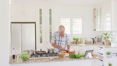 happy caucasian senior man using tablet and cooking in kitchen