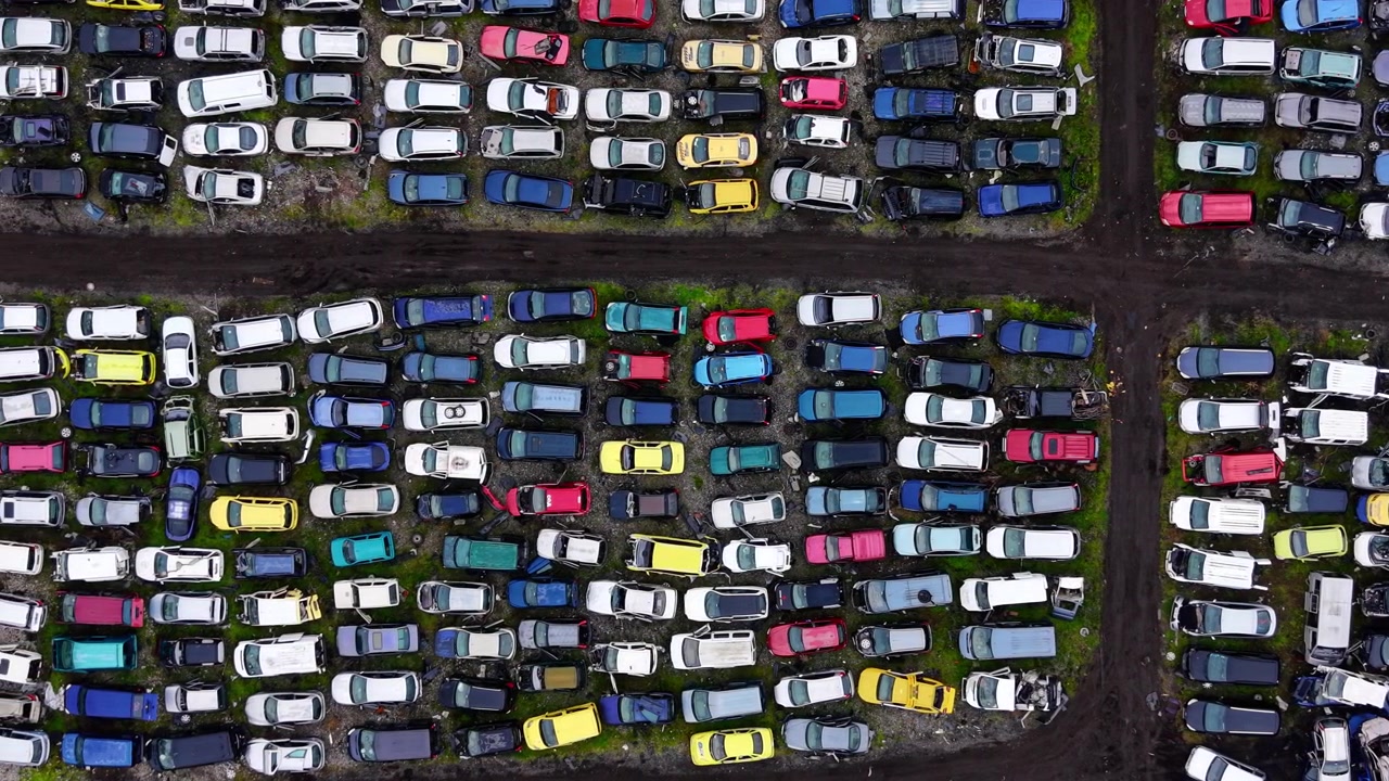 Luftfoto ovenfra af skrotbiler i fire sektioner, Bulgarien. Droneudsigt over farverige ødelagte køretøjer adskilt af mørke jordstier, der danner et krydsformet gitter.