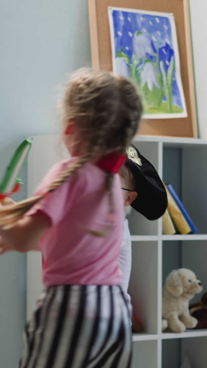 Couple of kids has fun at home. Toddler brother and preschooler sister run around and scream playing with toy swords. Children game of pirates