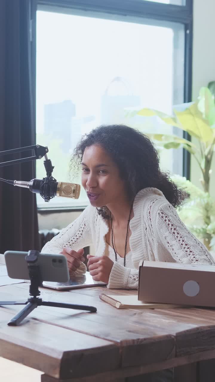 Young african american woman influencer speaks into microphone sits at table