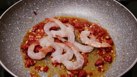 placing peeled shrimp in a frying pan where chorizo sausage and garlic are fried with oil