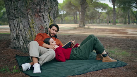 tender couple lying blanket at romantic forest picnic. man reading loud book