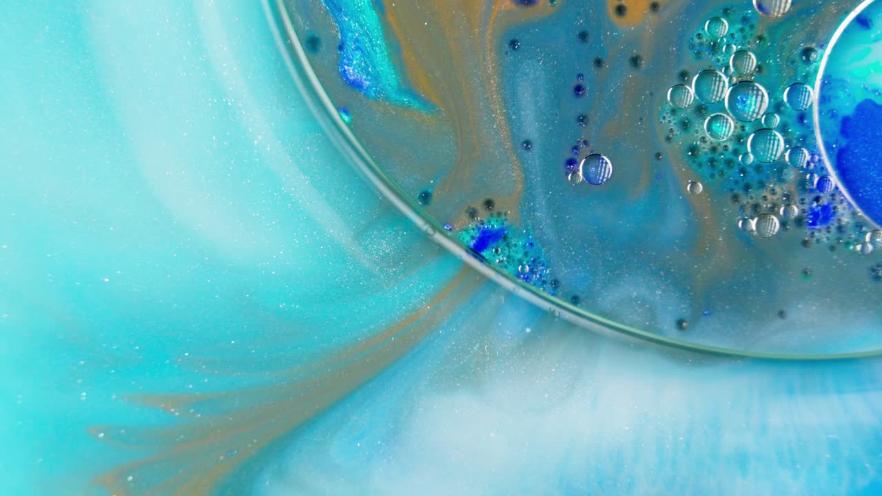 青、ターコイズ、黄土色の水彩インクの液体が泡立つ様子。