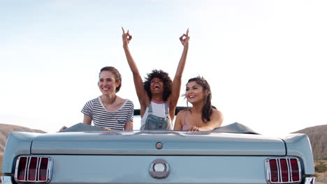 tres amigas en la parte de atrás de un coche clásico de tapa abierta