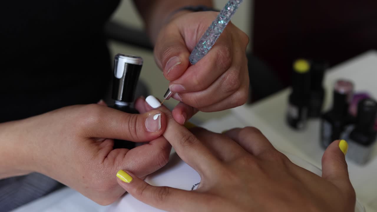 Anonymous beautician applying lacquer on female client nails