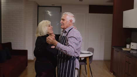 senior couple in love have romantic evening, dancing together in kitchen, celebrating anniversary