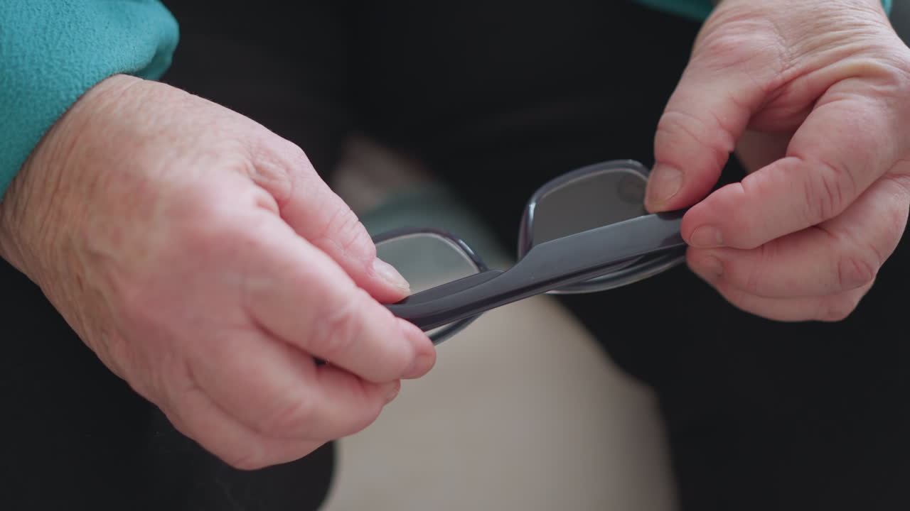 Lonely pensioner in green teal sweater adjusting glasses with both hands. Close-up shot of hands carefully adjusting eyeglasses, showcasing elderly person s routine of self-care and daily activity