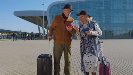 Senior-rich-pensioner-tourists-grandmother-grandfather-stay-near-airport-hall-hold-money-dollar-cash