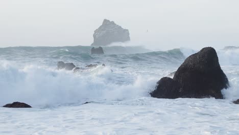 agua turbulenta llena de espuma blanca en la costa de islandia con formaciones de roca negra volcánica