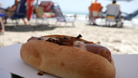 a hot dog topped with crispy onions next to the ocean