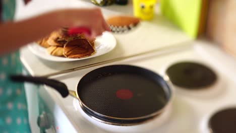 the girl's hands in a blue apron are removed from the pan of the pancake with a spatula. puts the pancakes in a pile.