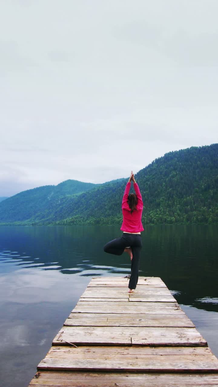 Woman practicing yoga on a wooden dock overlooking a serene lake and mountains
