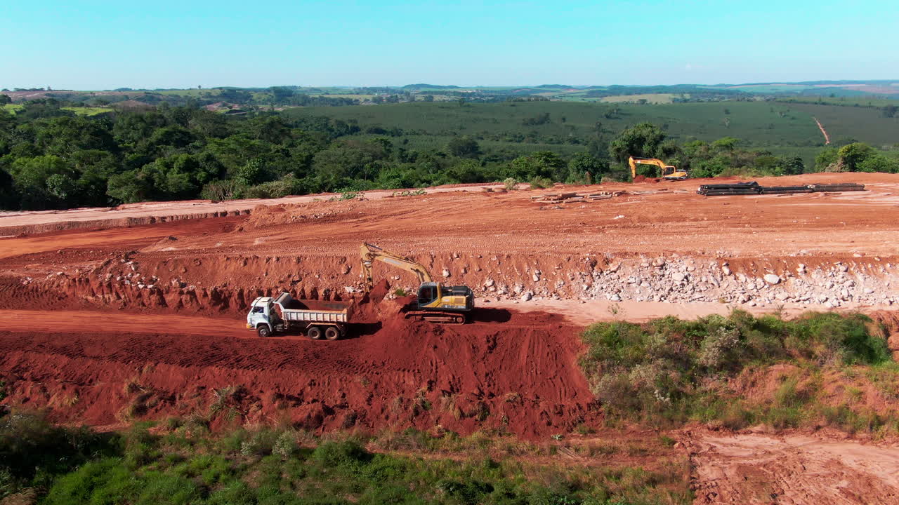Drone aerial landscape of dump truck reversing carrying soil to excavator digger machinery equipment at landfill tip site dirt mound in Brazil South America industry waste disposal operation