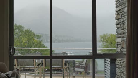 view from a wanaka hotel room during rain, showing balcony chairs and an approaching boat on the lake through a wet window