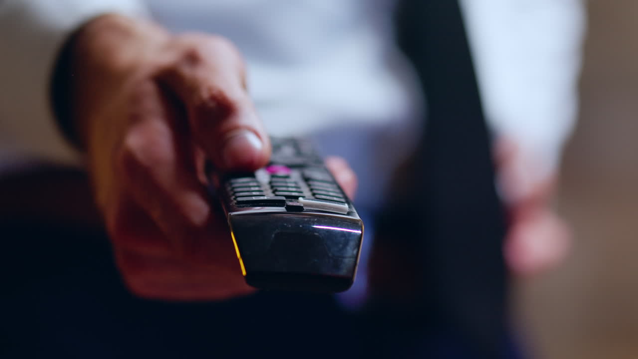 Close up of businessman relaxing after work using tv remote control