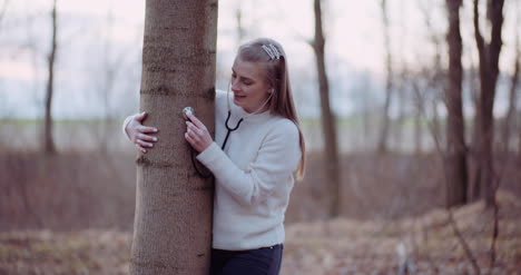 woman uses a stethoscope and examines a tree in the forest 4