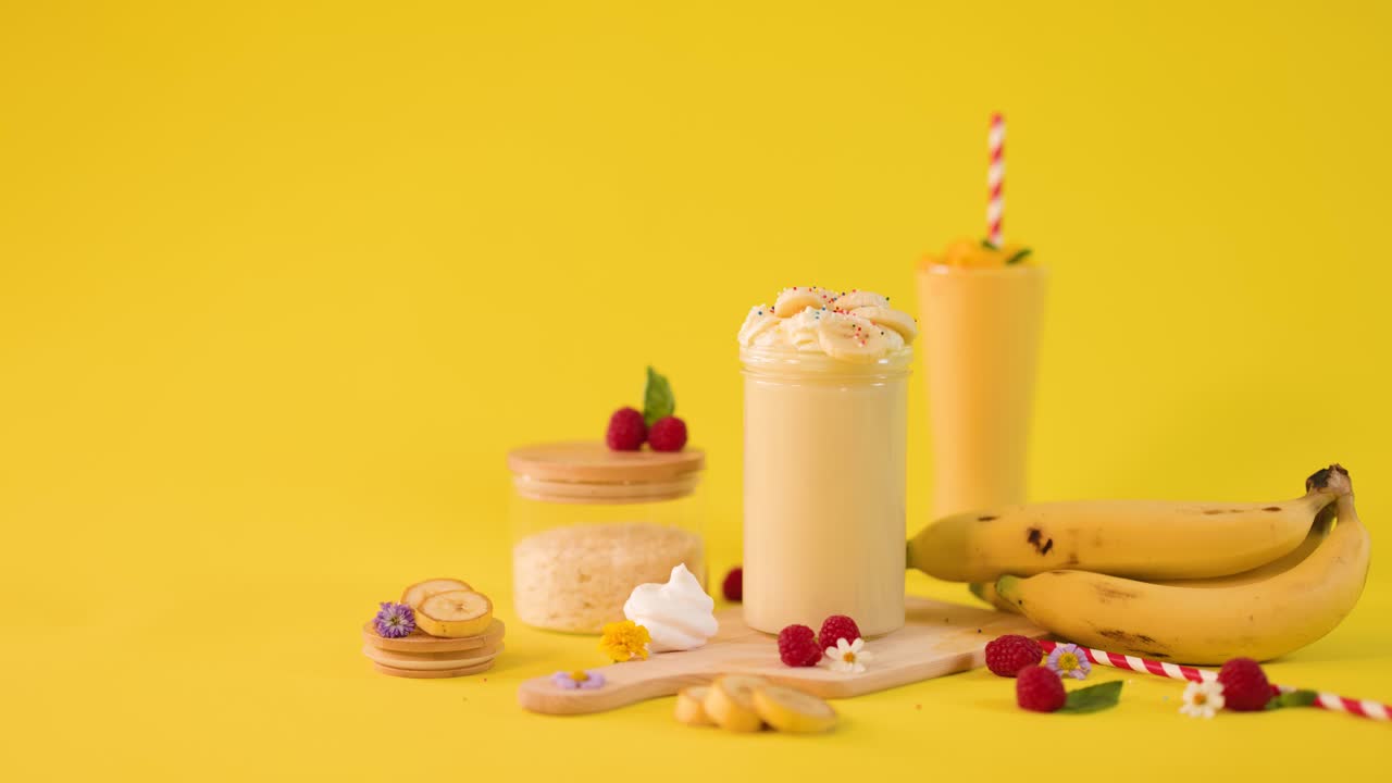 Una mano umana inserisce una cannuccia a righe in un cremoso frullato alla banana tra frutta e dessert tropicali
