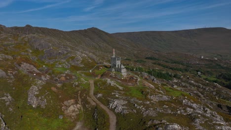 copper mine, allihies, county cork, ireland, september 2024. drone pushes in and orbits clockwise from a wide view of mountain slope towards the historic ruined engine house under a bright blue sky.