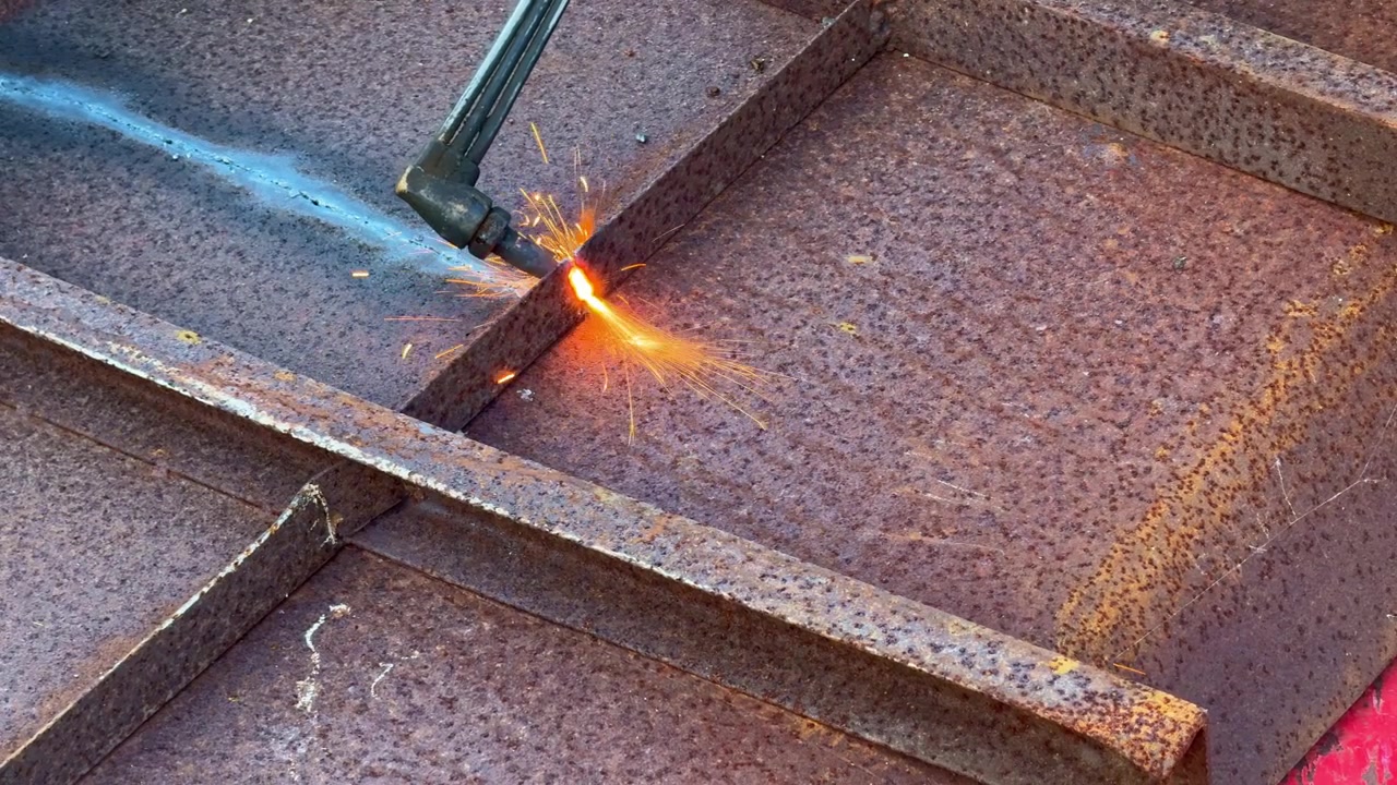 Industrial worker cuts a steel plate using a gas cutting torch. Close-up of metal fabrication, welding process, manufacturing, and engineering production.