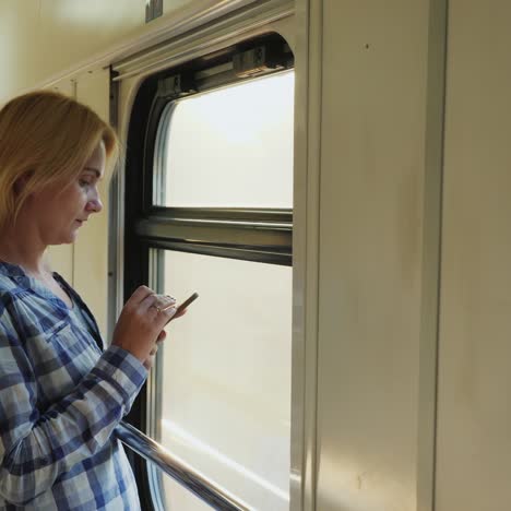 a woman uses a telephone in a train car, stands by the window