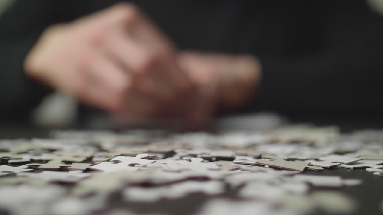 Puzzle pices falling on a table with a person's hands trying to solve the puzzle in the background. Shot in 4K, Slow Motion with Shallow Depth of Field