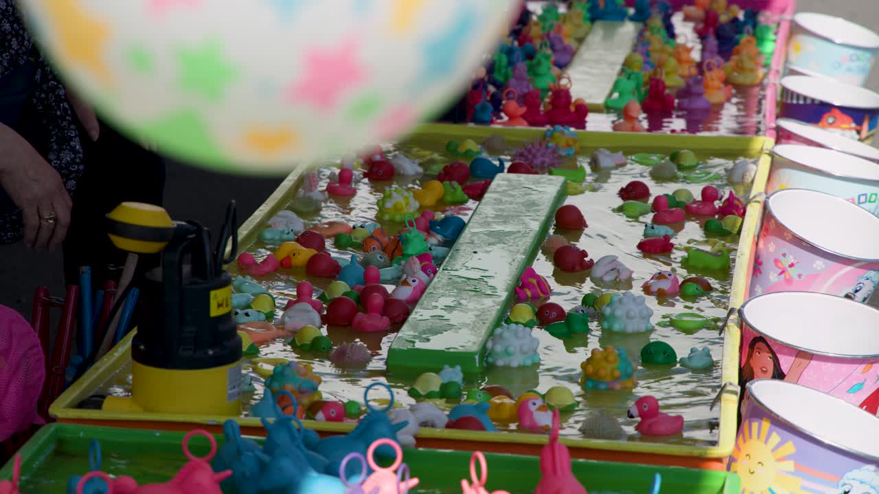 Brightly lit carnival game with floating plastic animals, buckets, and playful decorations, overhead camera movement