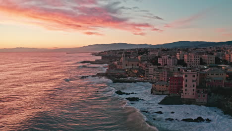 Vibrant-sunset-over-Genoa-Boccadasse-coastline-with-crashing-waves,-aerial-dolly