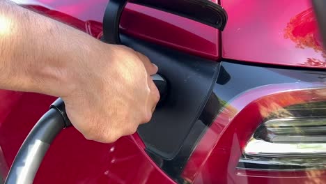 man unplugs the fast charger of red tesla electric vehicle charging port, close up