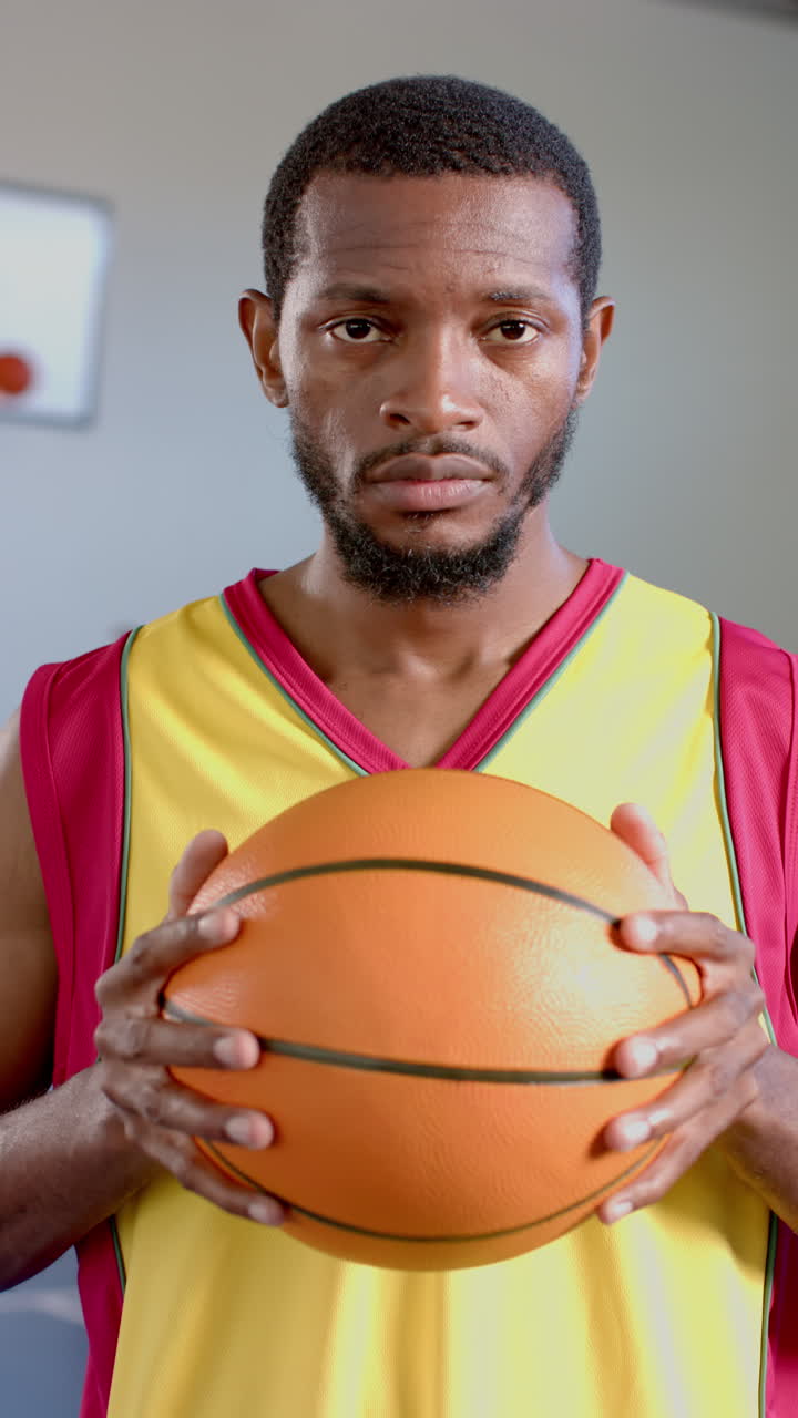 Vertical video: Holding basketball, man in sports jersey looking determined, ready for game