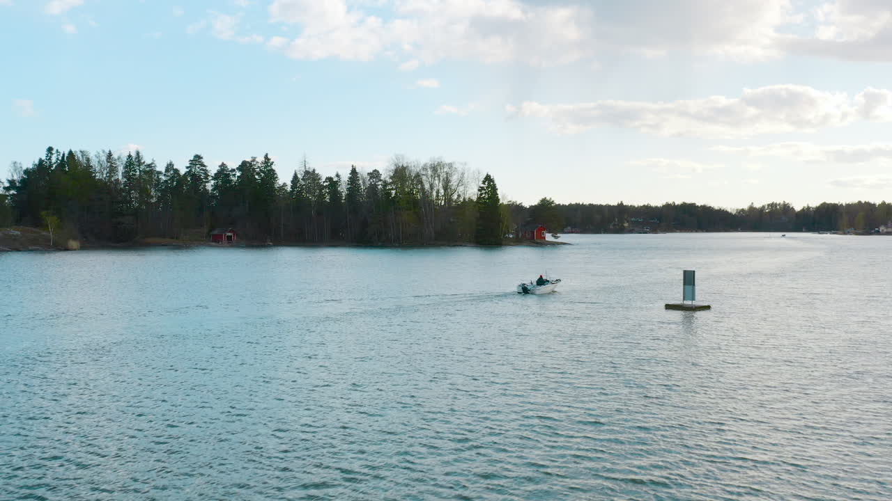 Rising from a water level view to a gently floating over a boat on beautiful blue waters with silhouettes of a Scandinavian forest.
