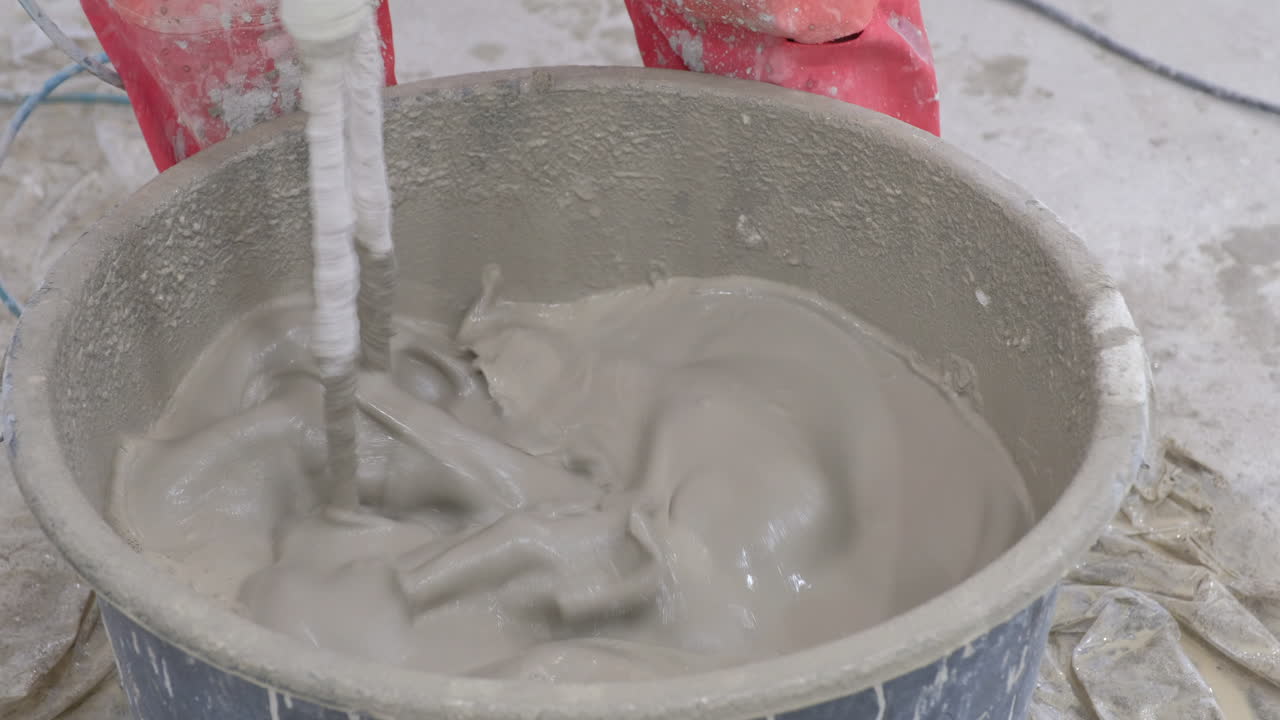 Mixing mortar in a round container A tool appears to be submerged in the mixture Red gloves are visible near the container's edge