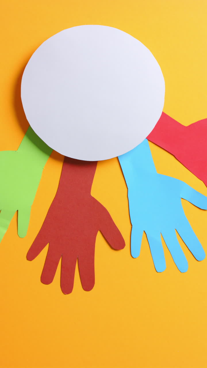Vertical video of hands around circle made of colourful paper on orange background with copy space