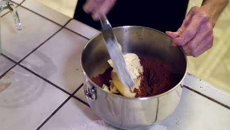 un chef en una cocina poniendo mantequilla vegana en un tazón de mezcla de metal mientras hornea un pastel de chocolate para el postre