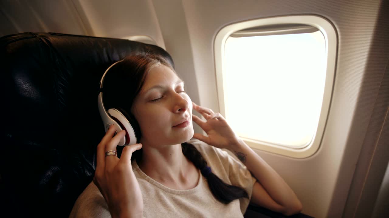 joven con auriculares inalámbricos escuchando música y sonriendo durante un vuelo en avión
