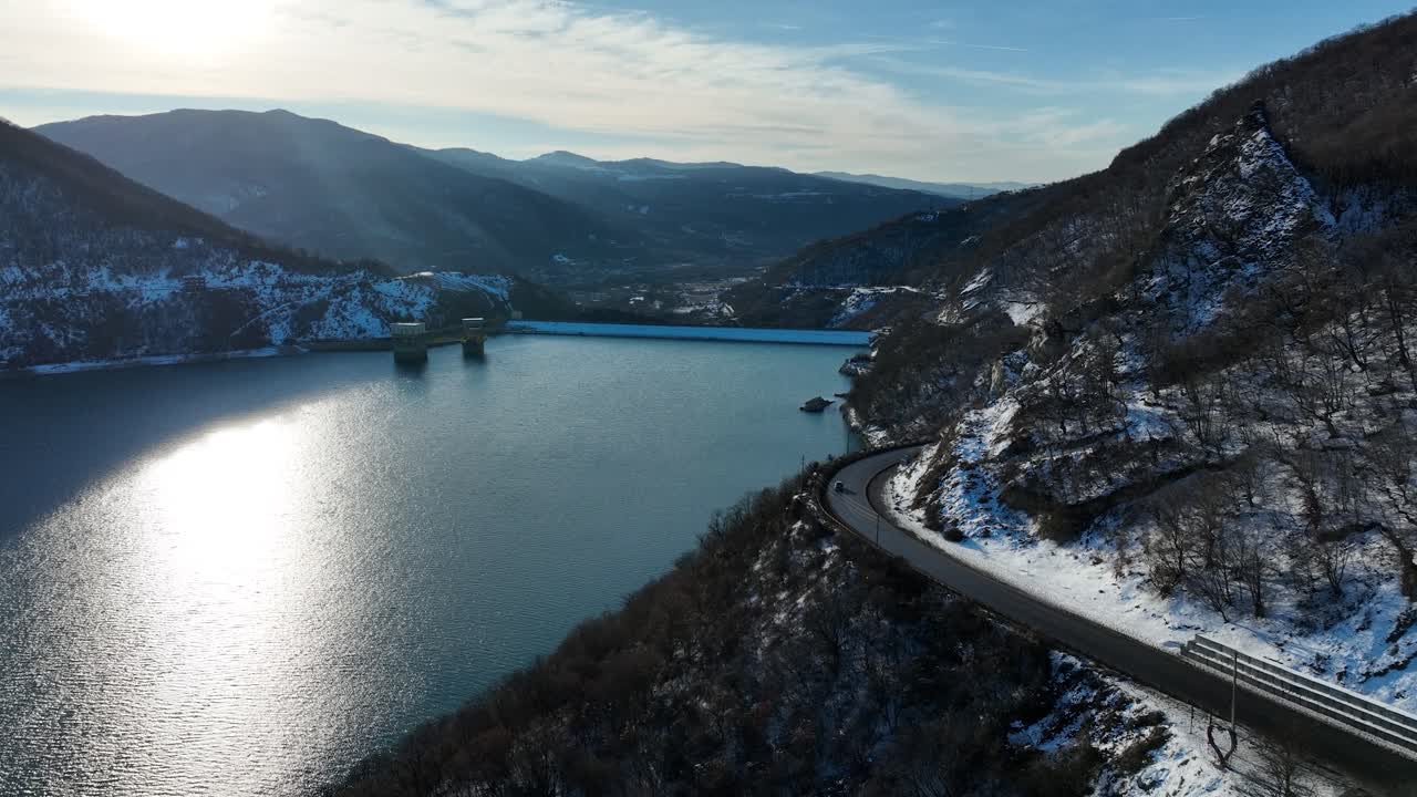 Una strada tortuosa costeggia il fianco di una collina innevata, conducendo a un ponte lontano e riflettendo la calma bellezza del fiume e delle valli circostanti