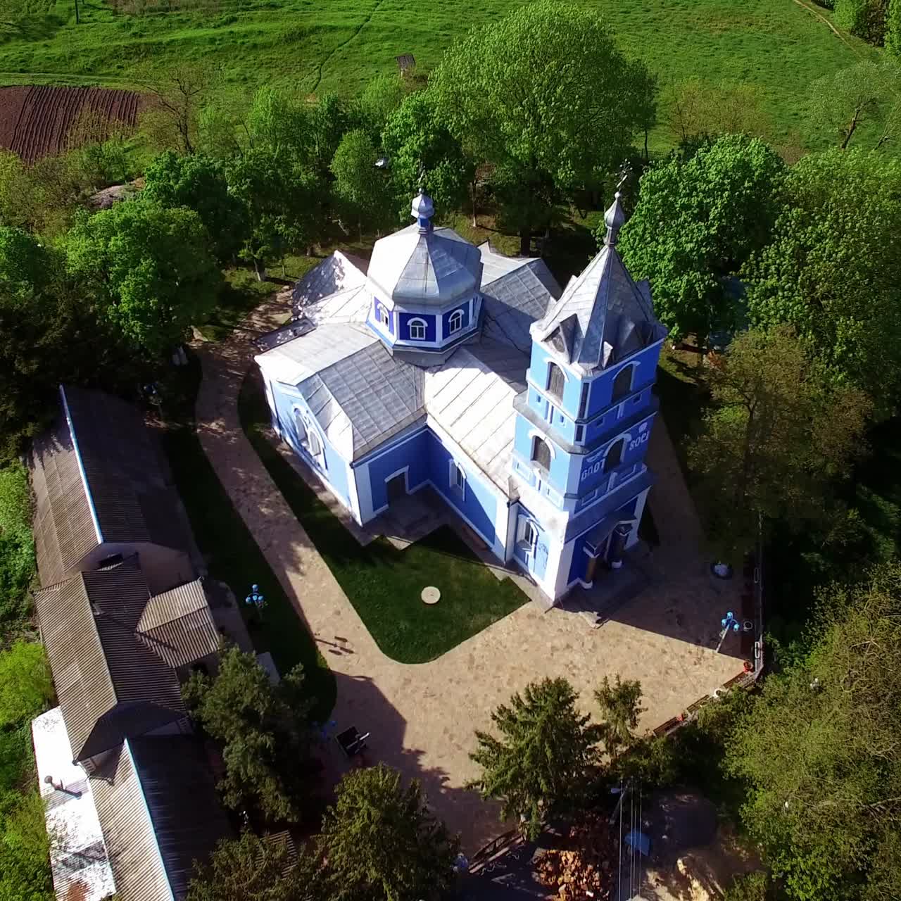 Beautiful building of a church surrounded by green trees. Drone circle movement over the building lit by bright sunshine. Top view