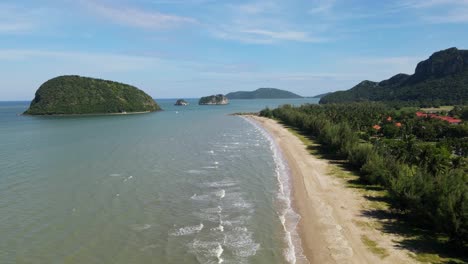 Steady-aerial-footage-from-a-high-altitude-revealing-waves-moving-towards-the-shore,-beachfront-and-roofs,-islands-and-blue-sky