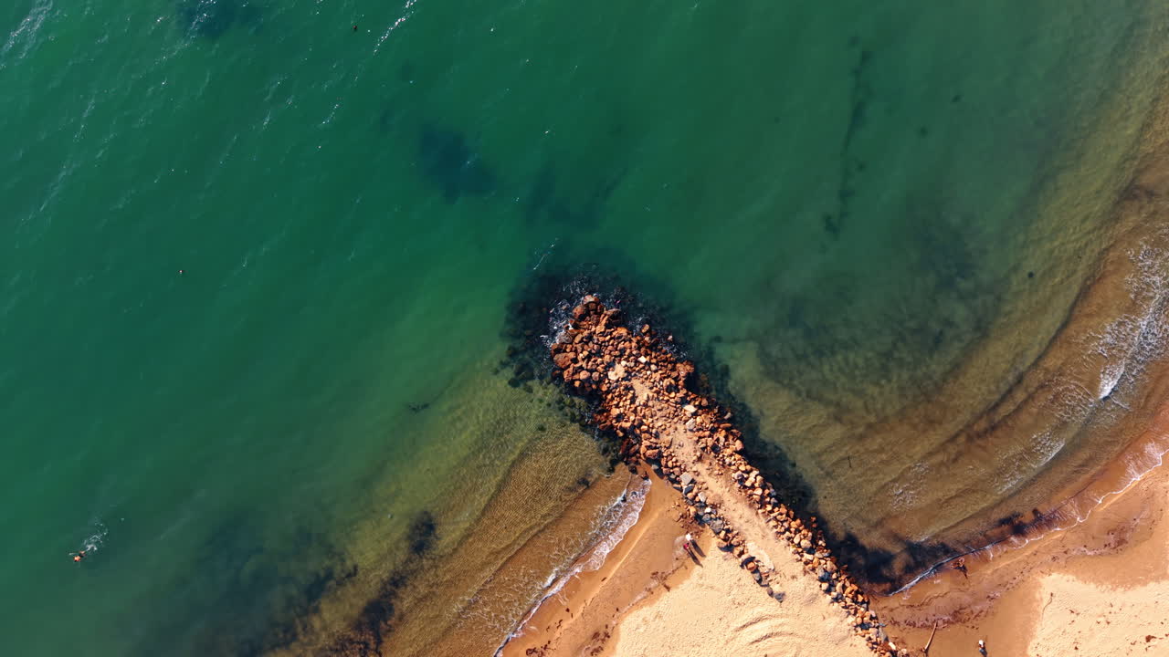 Bølgerne slår ind over klipperne på stranden under en solskinsdag ved havet. Bølgerne ruller ind mod klippeformationer på en strand