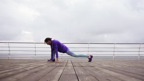 Young-athletic-woman-stretching-her-legs-before-her-training-on-the-beach-by-the-sea-early-in-the-morning.-Training-by-the-beach