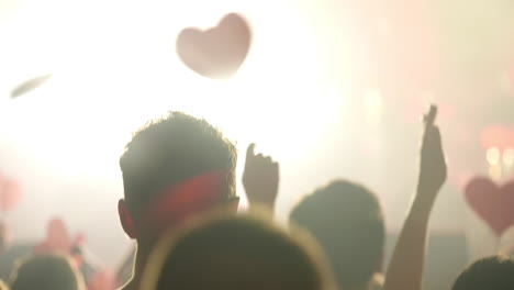 silhouetted crowd with hearts at a red-lit concert