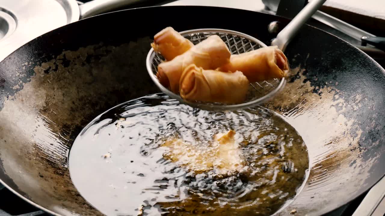Lumpia Asia panas telah selesai digoreng dalam wajan baja dan diangkat dengan saringan jaring logam berlubang, jarak dekat statis.