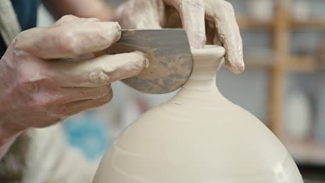 handmade ceramic. male artist smoothing out neck on ceramic vase, using spatula nd pottery wheel, close up, slow motion