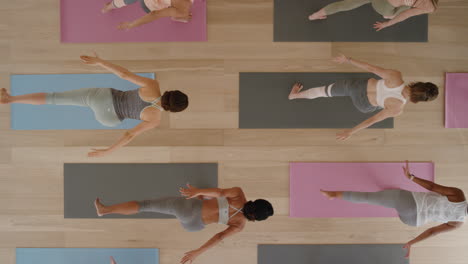 Vista-Superior-Clase-De-Yoga-Mujeres-Sanas-Practicando-Pose-Guerrera-Disfrutando-Del-Estilo-De-Vida-Físico-Haciendo-Ejercicio-En-El-Gimnasio