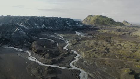 aerial drone over glacial river towards melting glacier covered in black volcanic ash