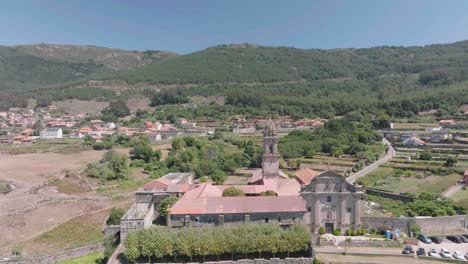 aerial drone forward moving shot over a damaged historic monastery called santa maria de oia with bell tower on the foothills of a mountain range